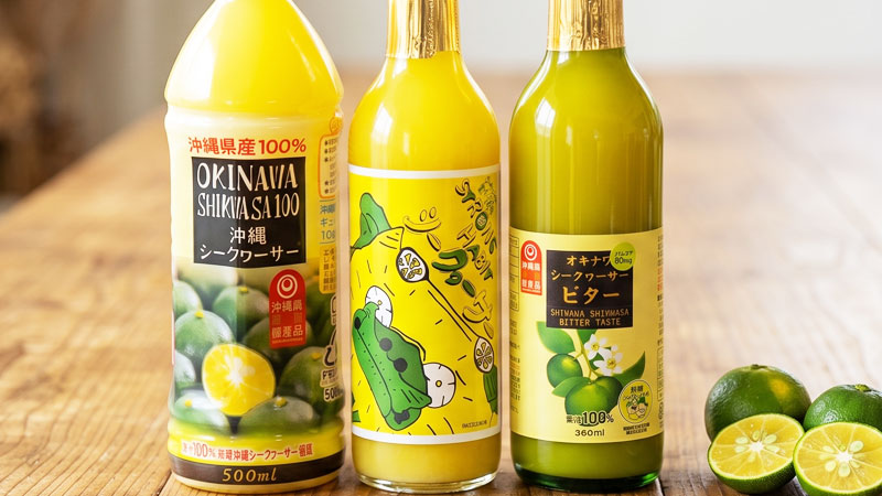 3つのシークヮーサー果汁100%ボトルとシークヮーサーの実・花が綺麗に並んだ全景